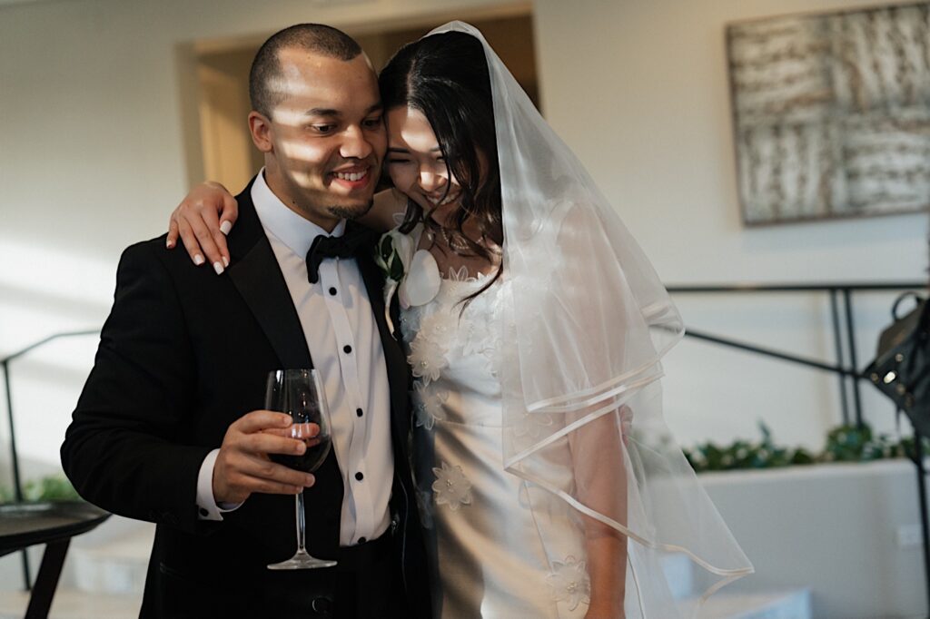 Bride and Groom hug while holding wine glasses at wedding reception at Four Seasons Oahu in Hawaii. 