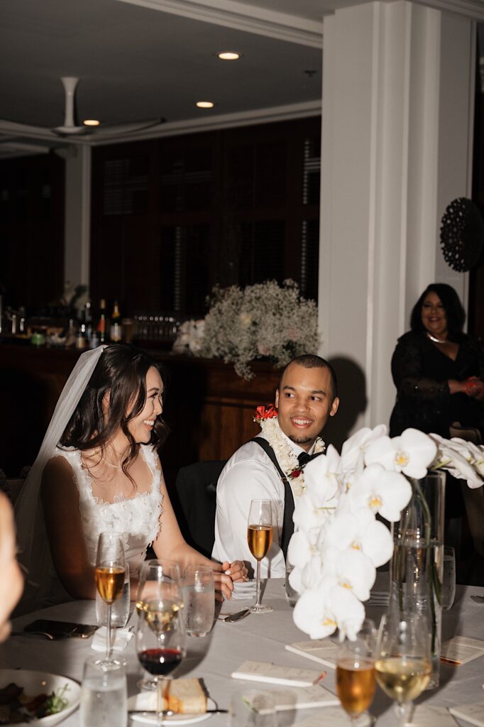 Bride and Groom sitting together at reception table smile at each other at Four Seasons Oahu in Hawaii. 