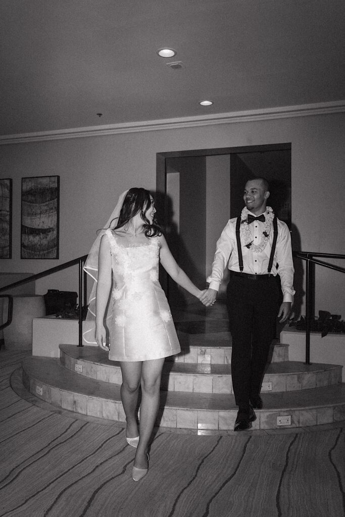 Black and White photo of bride standing in short reception dress holding hands and looking at groom at Four seasons Oahu in Hawaii 