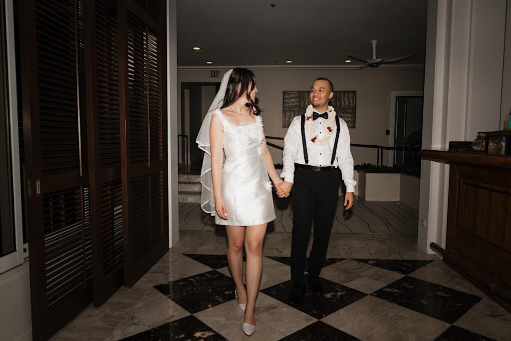 Bride standing and walking in short reception dress holding hands and looking back at groom in Hawaiian Lei at Four seasons Oahu in Hawaii 