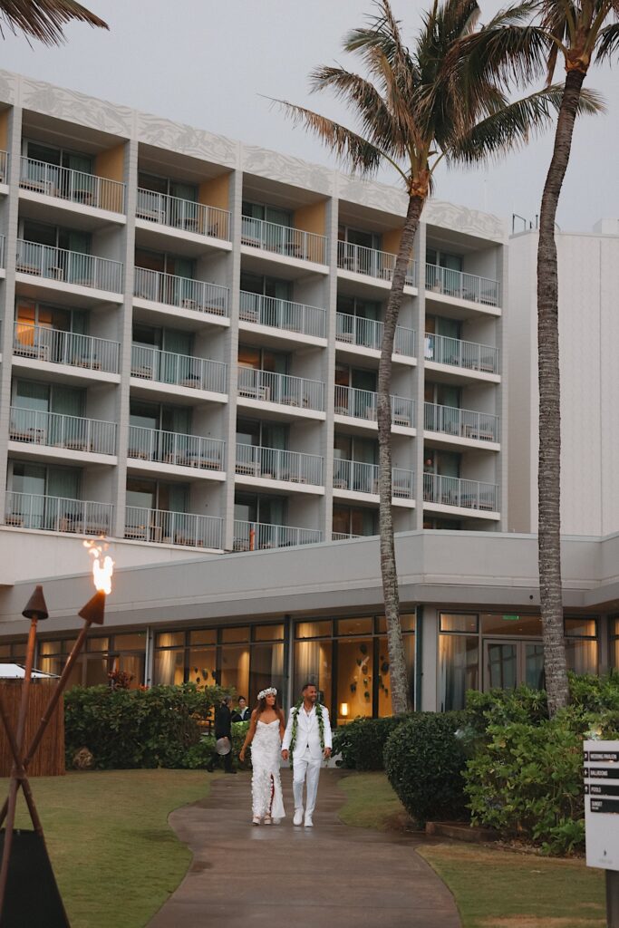 Bride with beautiful dress and lei headpiece and Groom walk with the Turtle Bay hotel in the background. 