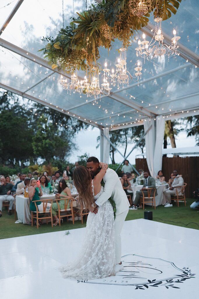 Bride and groom dance on dance floor under clear tent with chandeliers hanging during reception at Turtle Bay wedding venue. 