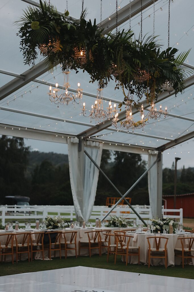 Clear tent with chandeliers hanging from the ceiling and beautiful classic tables sitting underneath for reception on Turtle Bay in Oahu Hawaii. 