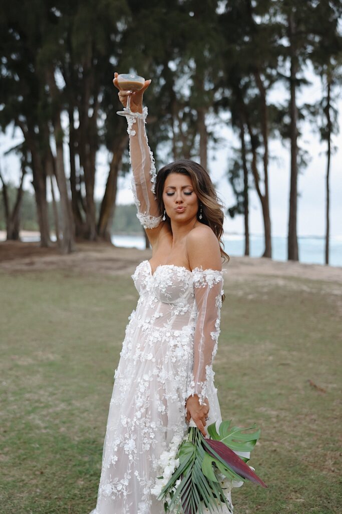 Bride in floral dress holds up espresso martini outside of wedding reception near the beach at Turtle Bay Wedding Venue in Oahu, Hawaii.