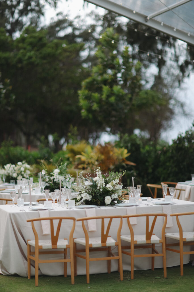 Hawaii wedding photographer captures wedding tables set with wooden chairs and large white and green centerpieces. 