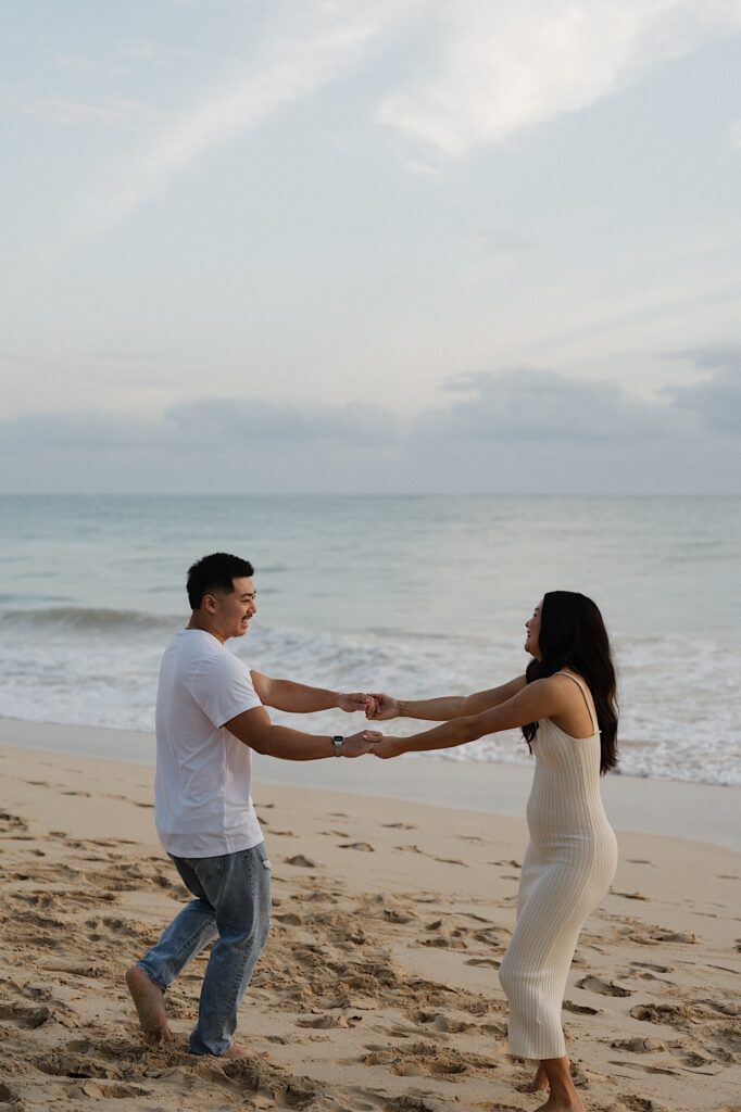 A couple hold hands and smile at one another while spinning in a circle during sunrise on Waimanalo Beach