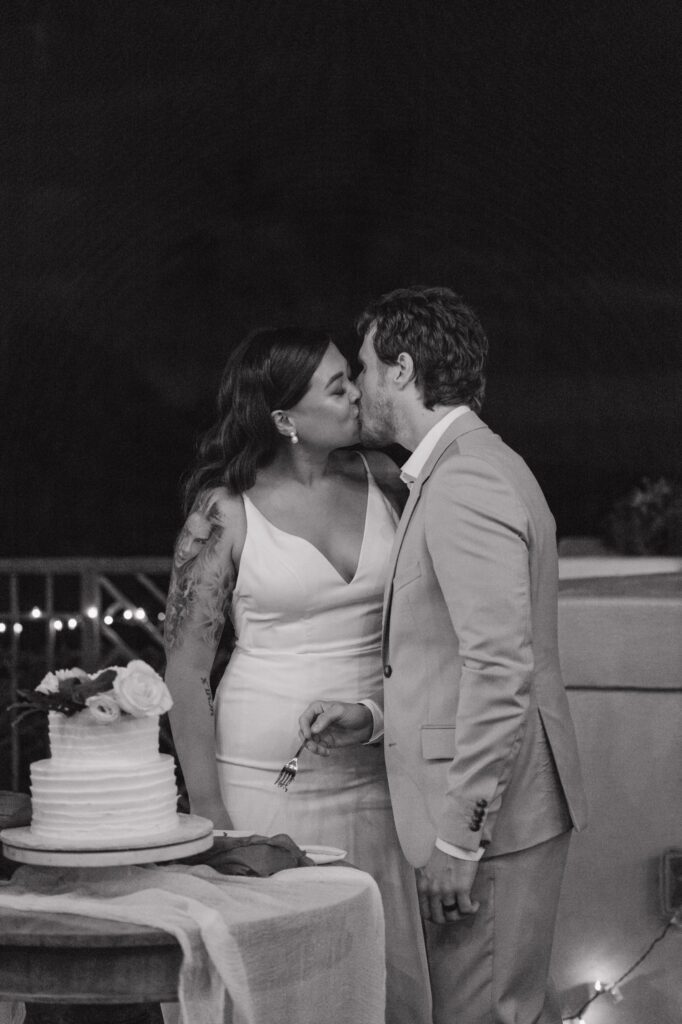 A bride and groom kiss on their wedding day during their outdoor wedding reception at Gather on Maui.  They are eating and cutting the cake during their reception.  